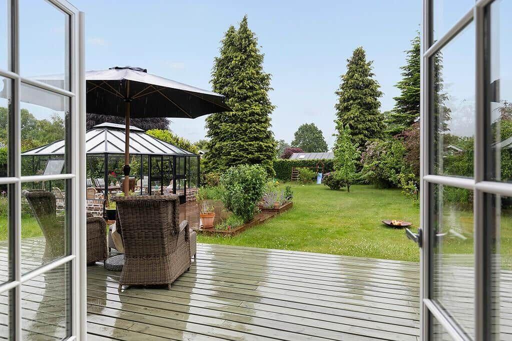 Terrasse mit Sitzgelegenheiten und Garten mit Bäumen und Beeten.
