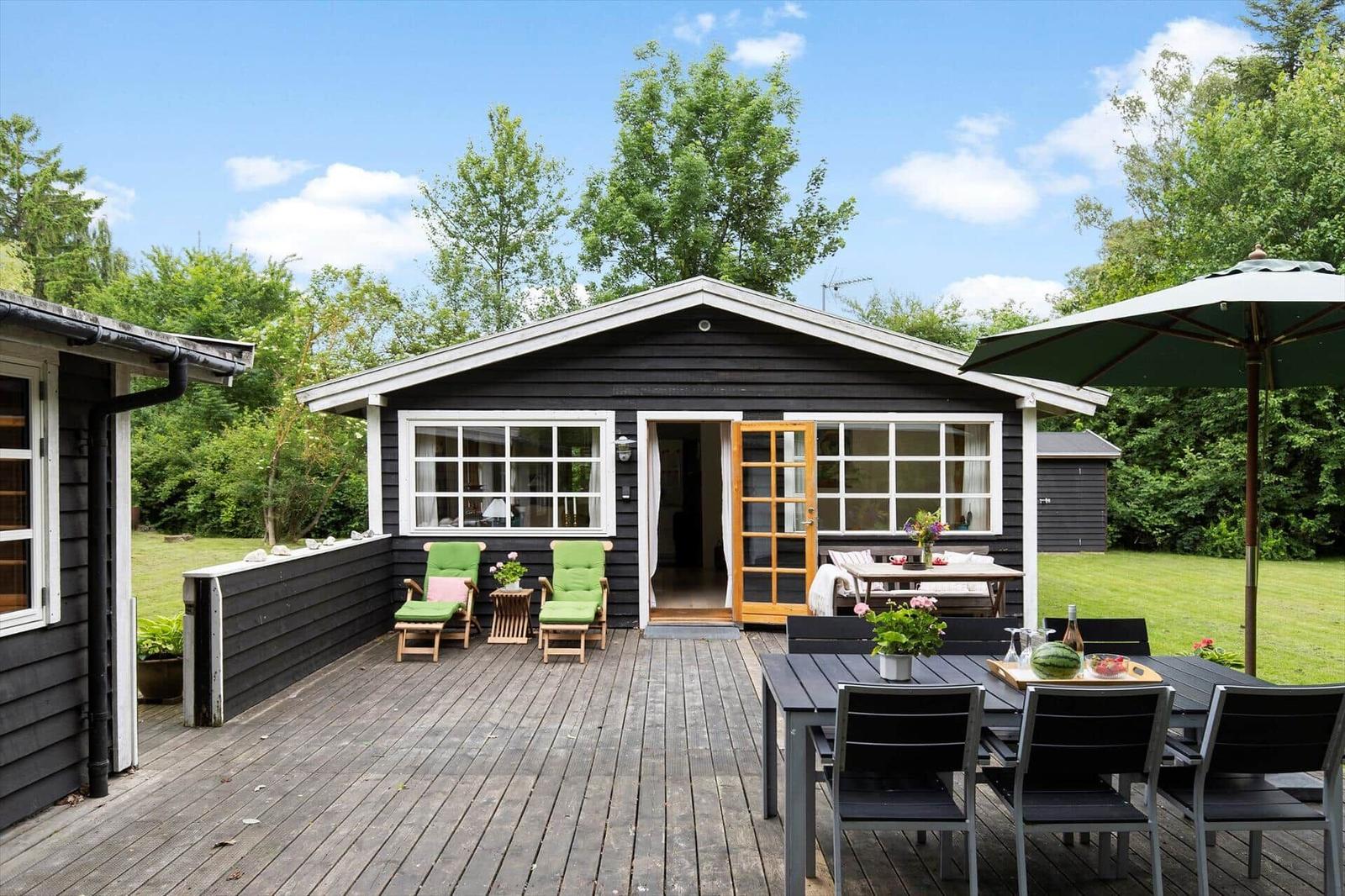 Schwarzes Holzhaus mit Terrasse, Garten und Sitzgelegenheiten.