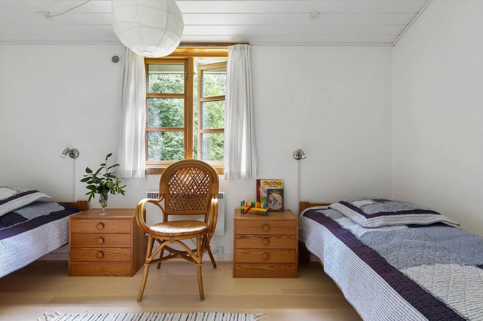 Zwei Betten, ein Stuhl und ein Fenster mit Blick auf Bäume.