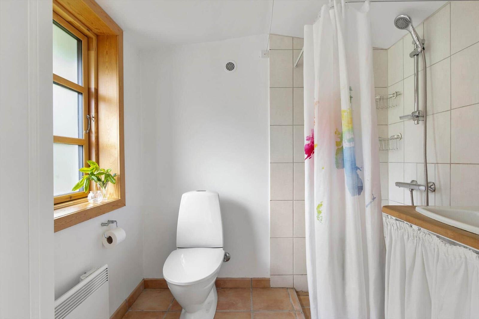 Badezimmer mit Toilette, Dusche und Fenster mit Pflanze.