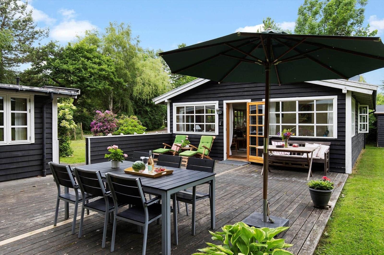 Terrasse mit Tisch, Stühlen und Sonnenschirm vor einem Haus mit dunkler Fassade.