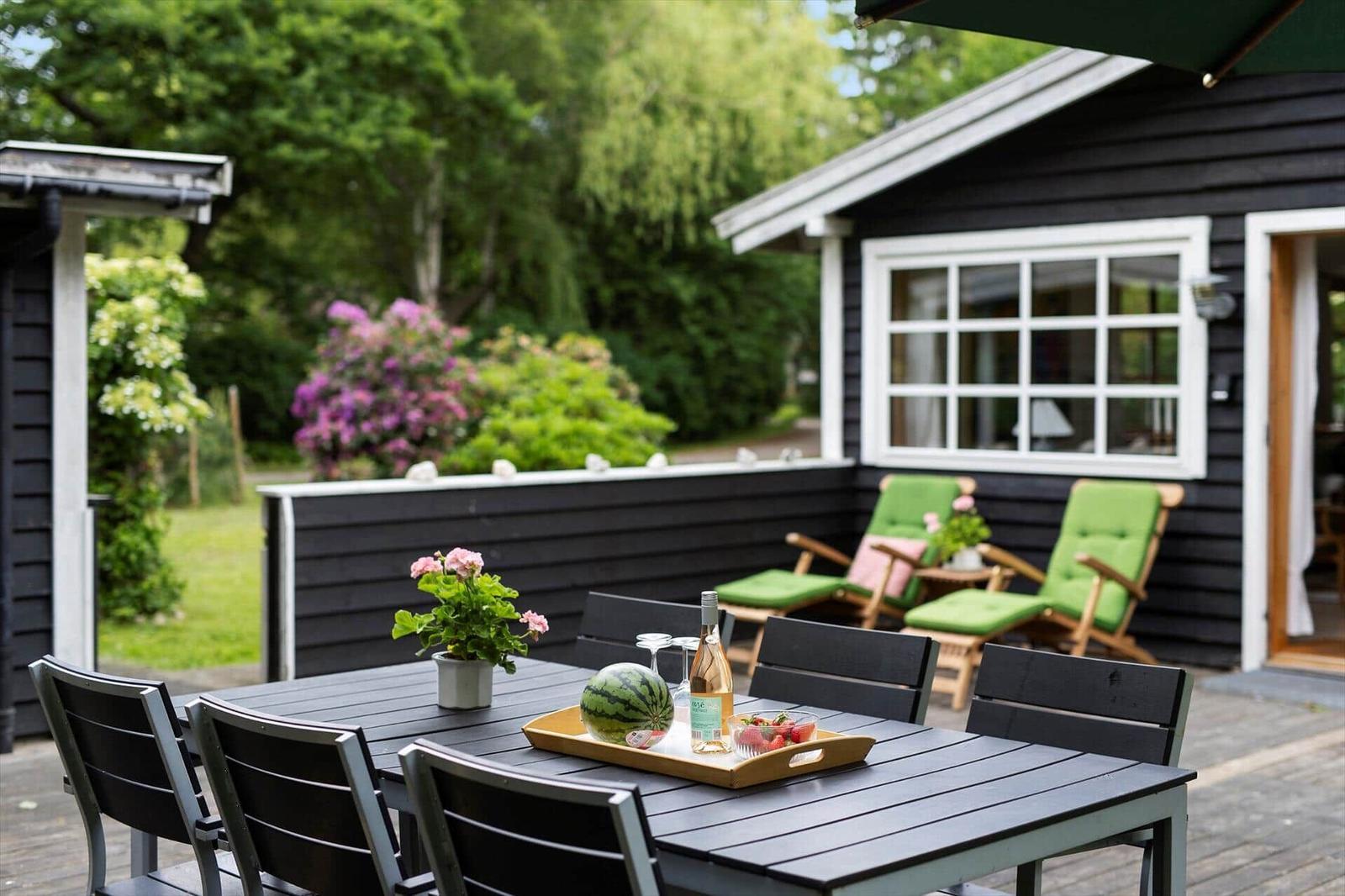 Terrasse mit Tisch, Stühlen und grünen Sesseln. Hintergrund: Haus mit Fenstern und Garten.