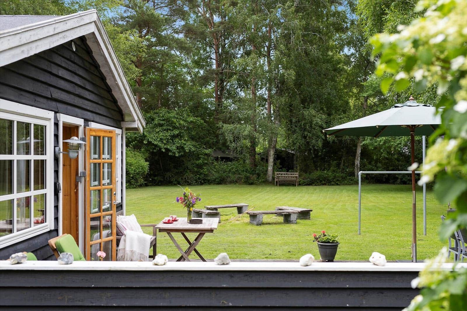 Hinter dem Haus befindet sich ein großer Garten mit Tisch, Bänken und Sonnenschirm.