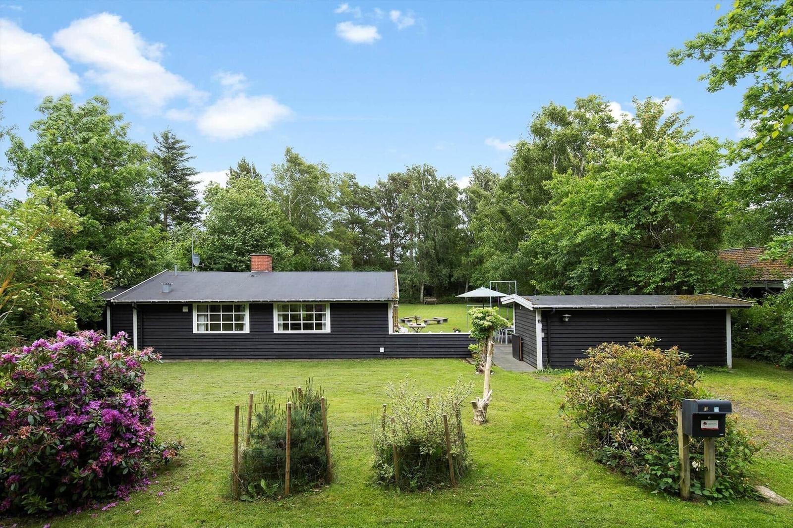 Schwarzes Holzhaus mit Garten, Grillplatz und Bäumen im Hintergrund.