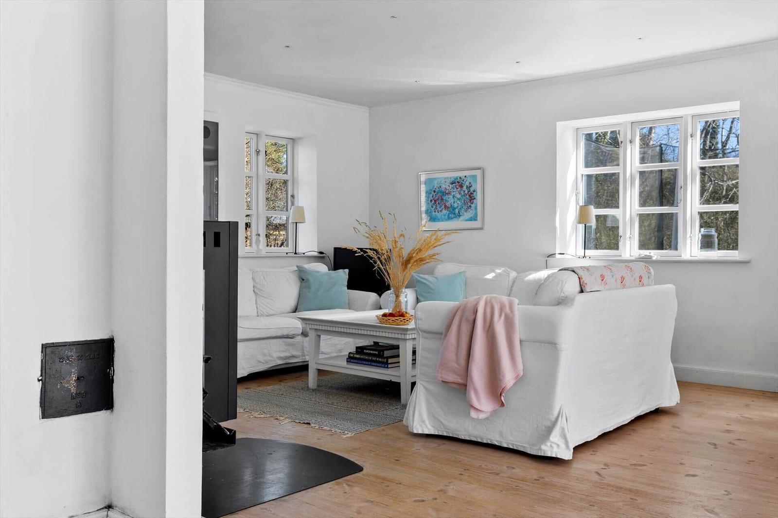 Wohnzimmer mit weißem Sofa, Holzboden und Fenstern. Es gibt einen Kamin und eine Couch.