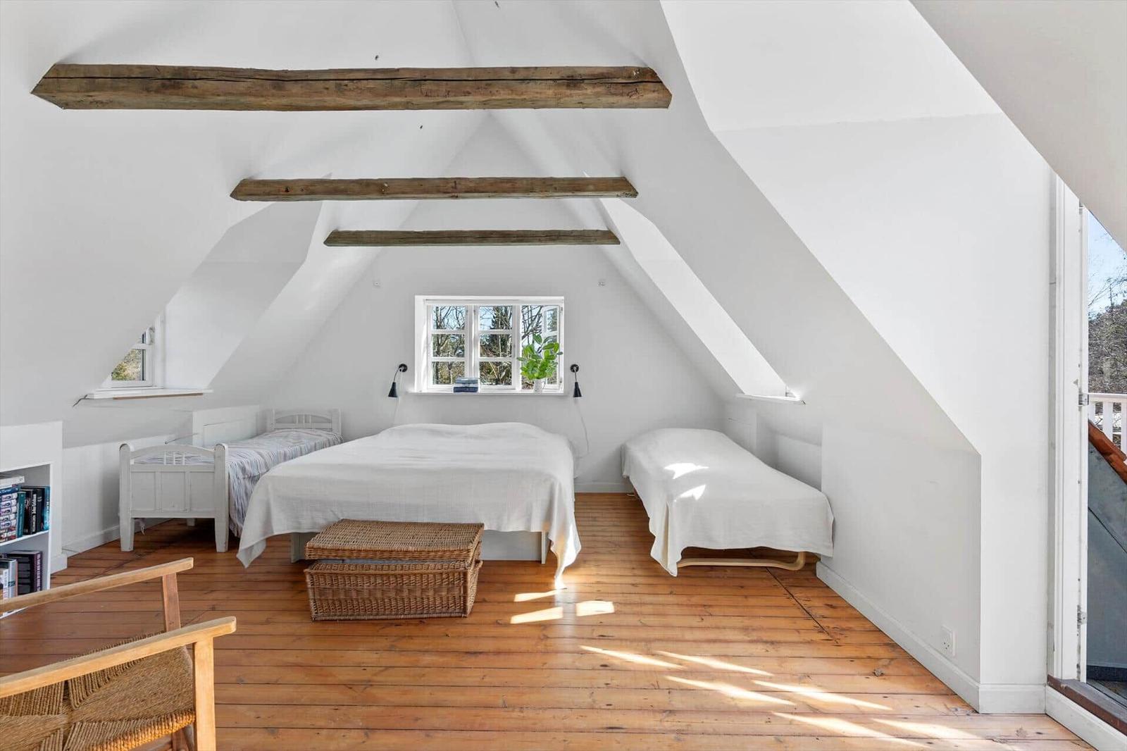 Schlafzimmer mit Dachschrägen, Holzboden und drei Betten. Fenster und Balkonzugang.