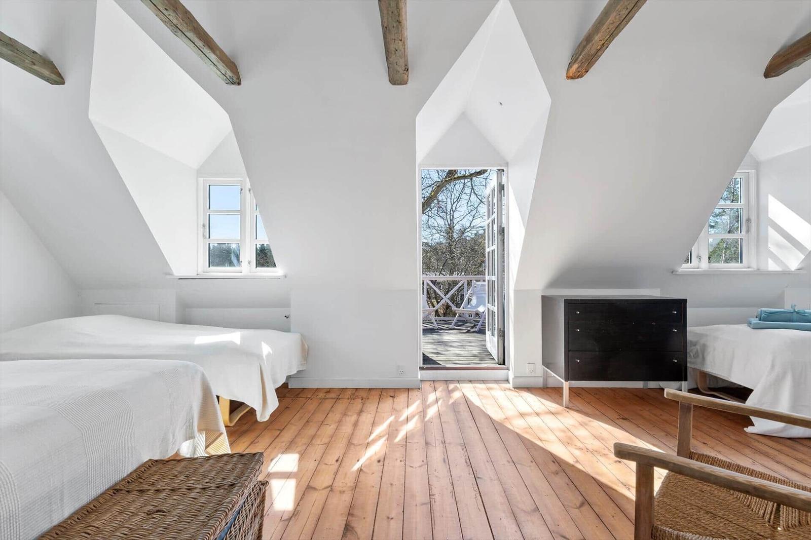 Zwei Betten, Holzfußboden, Dachschrägen und Fenster mit Blick auf Balkon.