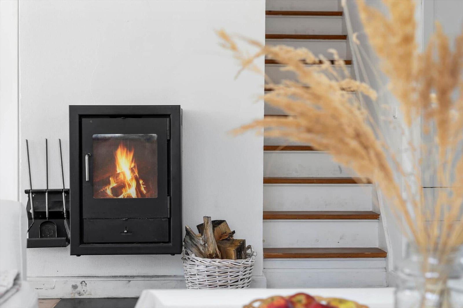 Wandofen mit brennendem Feuer, Kaminholz im Korb und Treppe mit Holzstufen.