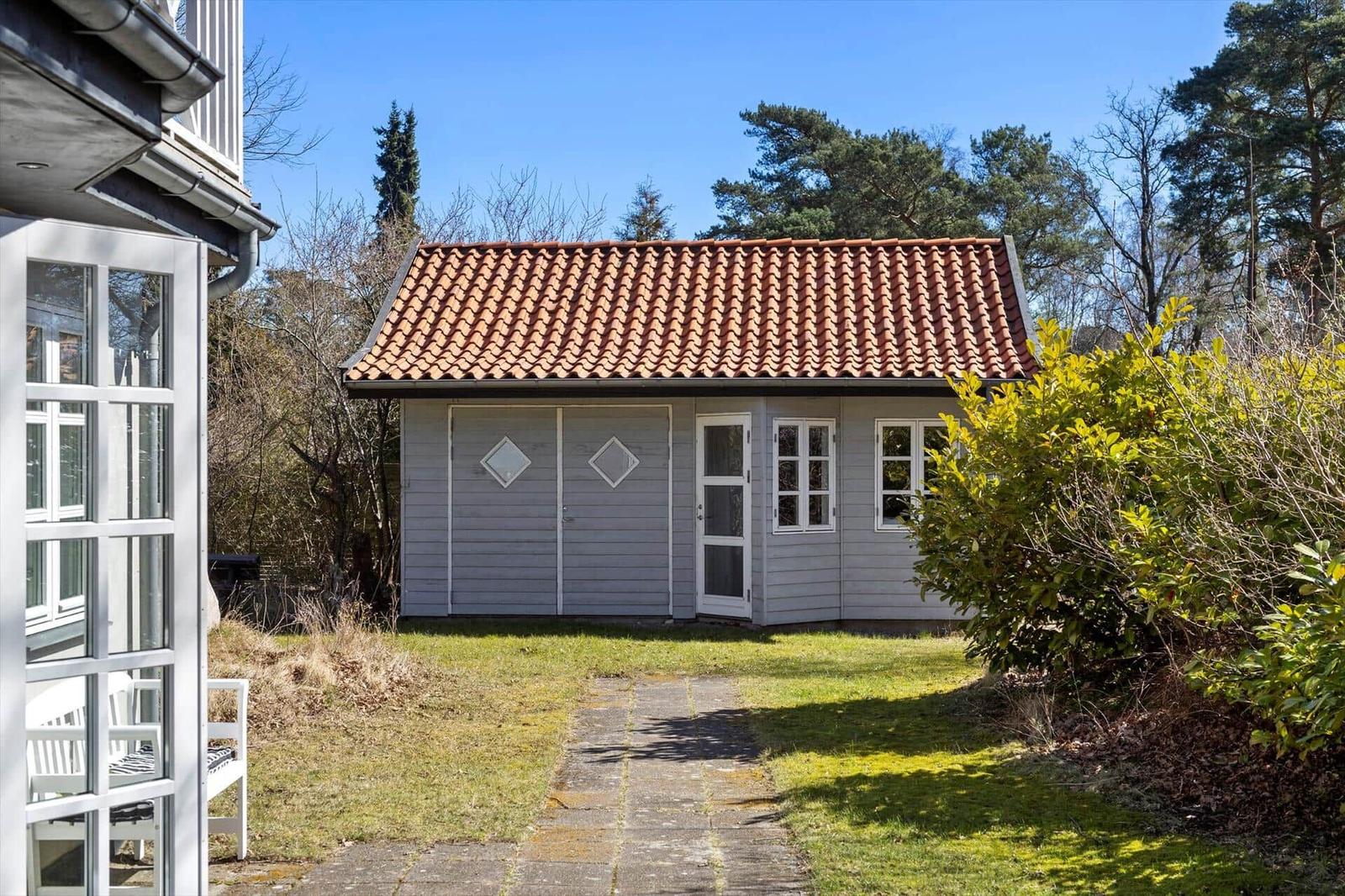 Ein kleines Haus mit rotem Ziegeldach und weißer Tür im Garten.