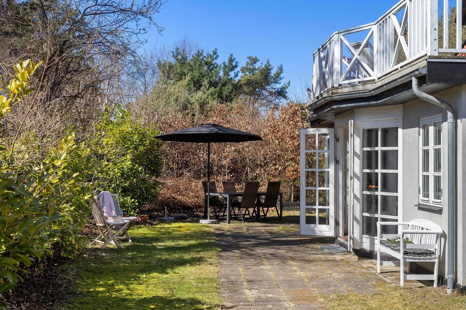 Haus mit Terrasse, Garten, Sitzgelegenheiten und Sonnenschutz.