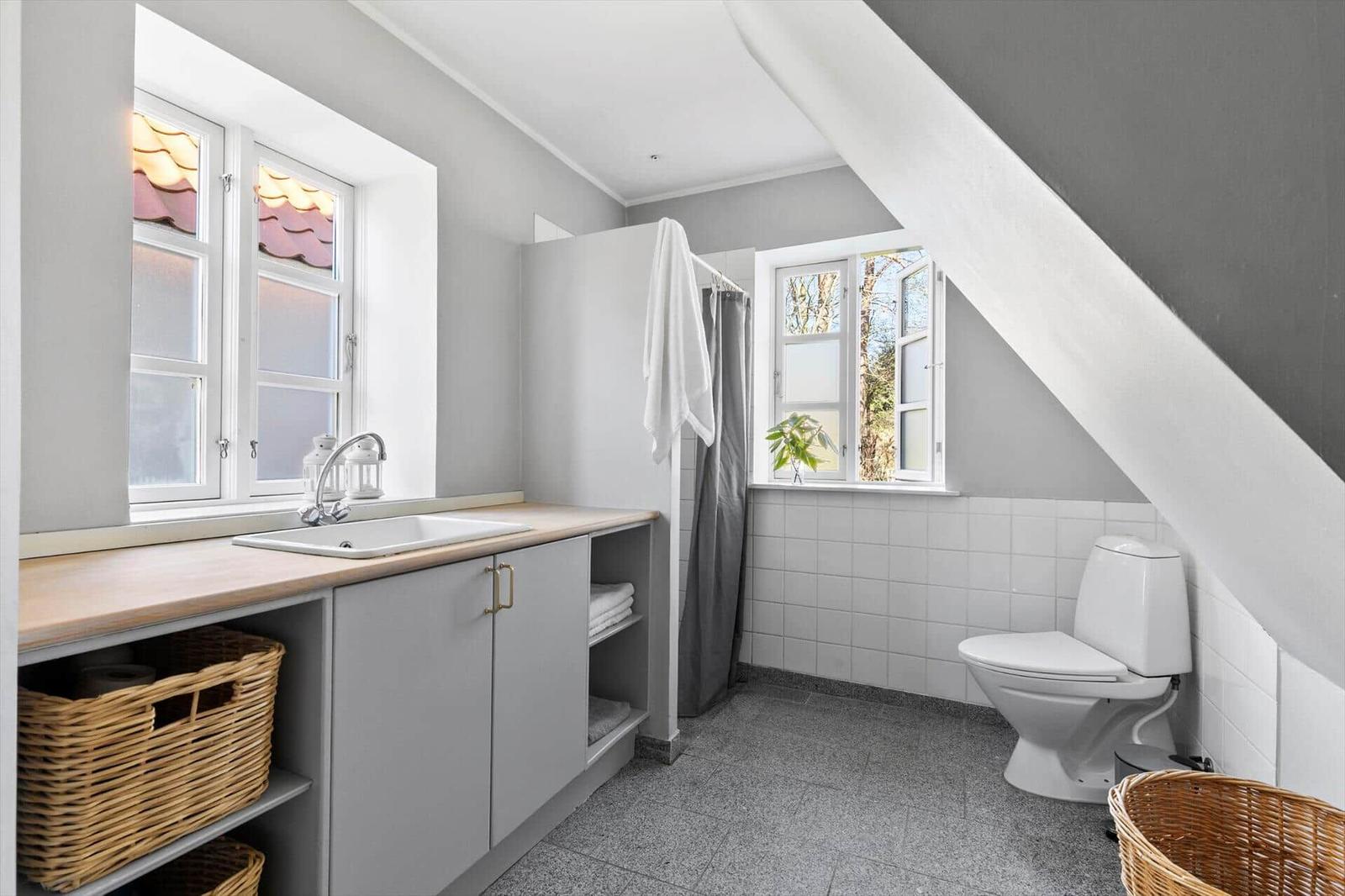 Badezimmer mit Waschbecken, Toilette und Dusche unter Dachschräge.