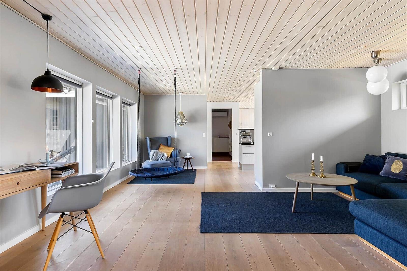 Wohnraum mit Holzboden, blauem Sofa und Schaukelstuhl. Küche und Arbeitsplatz sind sichtbar.