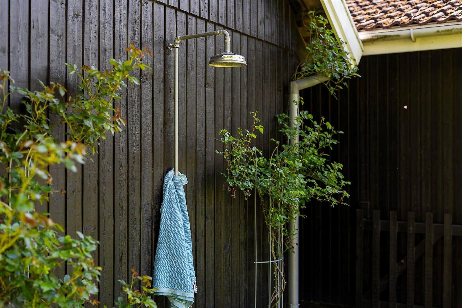 Außendusche an Holzwand mit Handtuch und Pflanzen