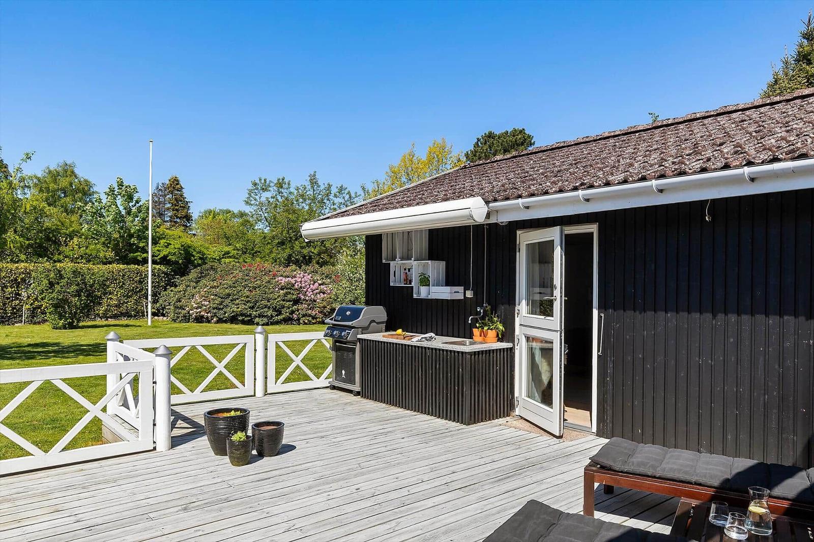 Terrasse mit Grill, Küchenzeile und Liegestühlen neben einem schwarzen Haus.
