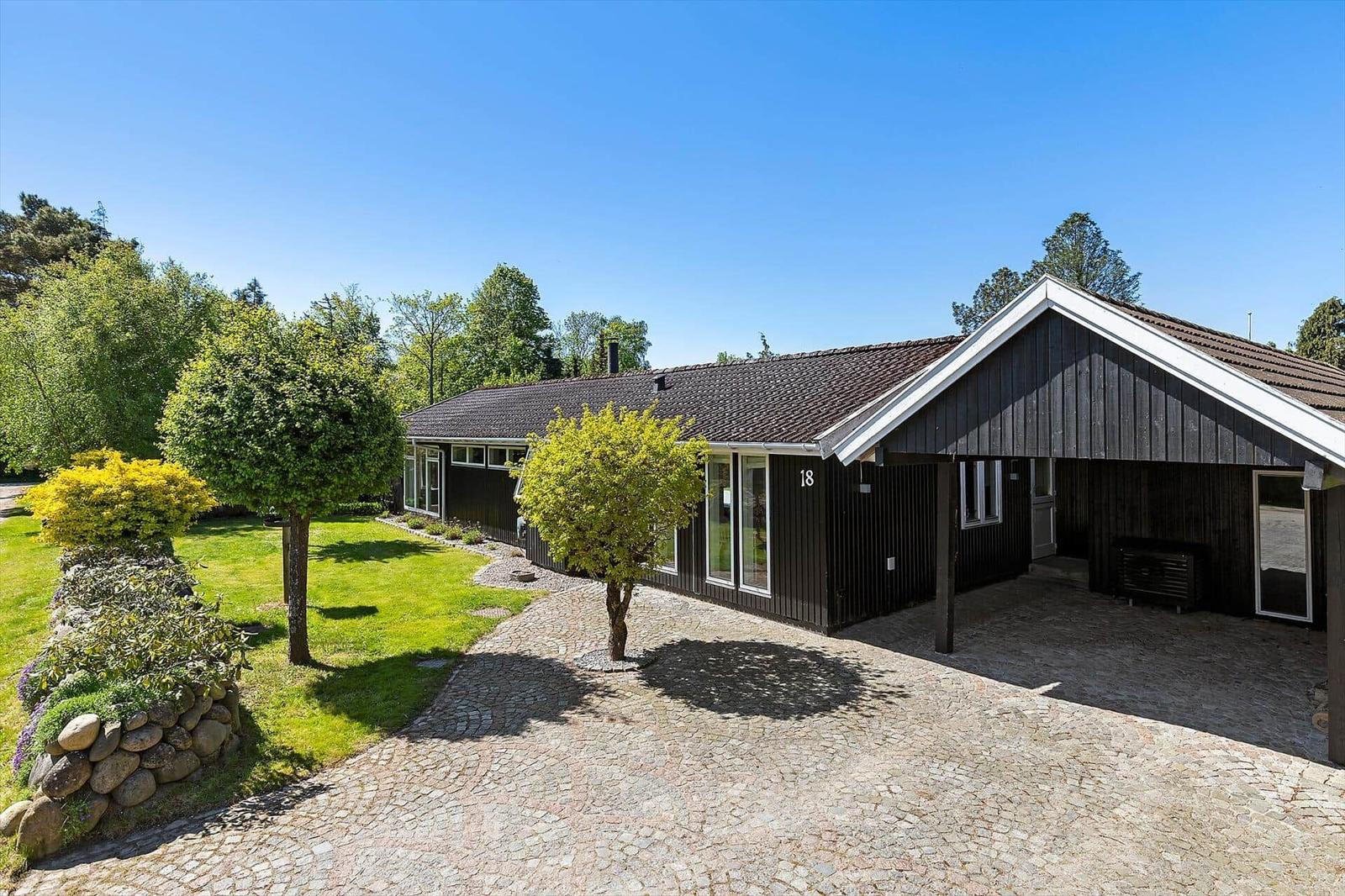 Schwarzes Holzhaus mit Steinweg und Garten. Nummer 18. Klare Sicht auf das Gebäude.