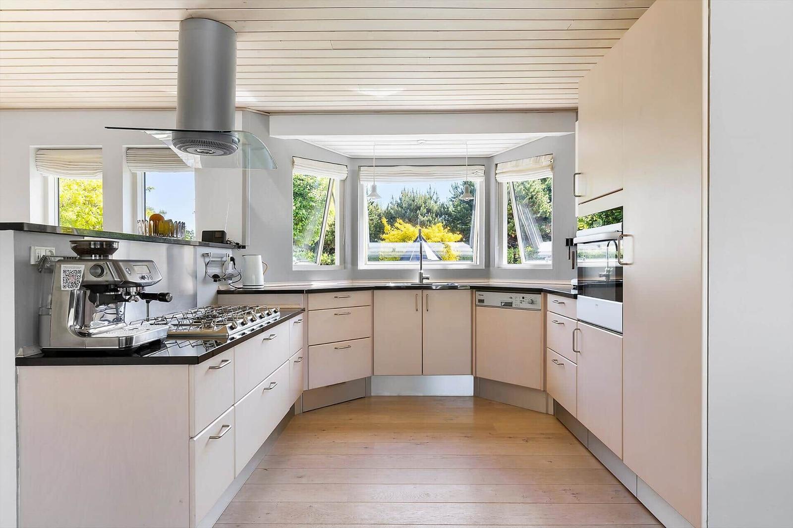 Moderne Küche mit Holzboden, hellen Schränken und Blick auf grüne Bäume.