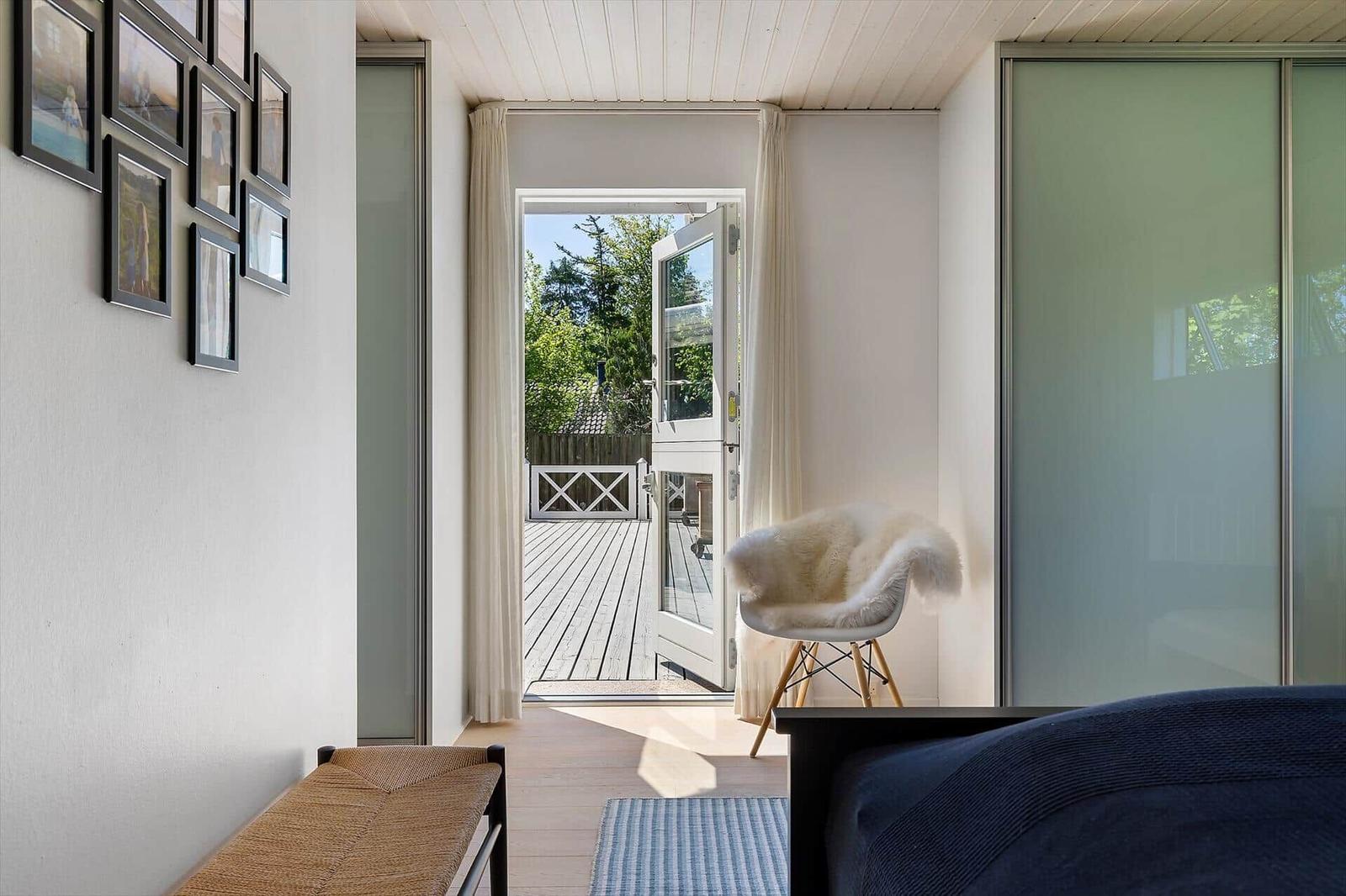 Schlafzimmer mit Blick auf Terrasse, Stuhl mit Fell, Wand mit Bildern.