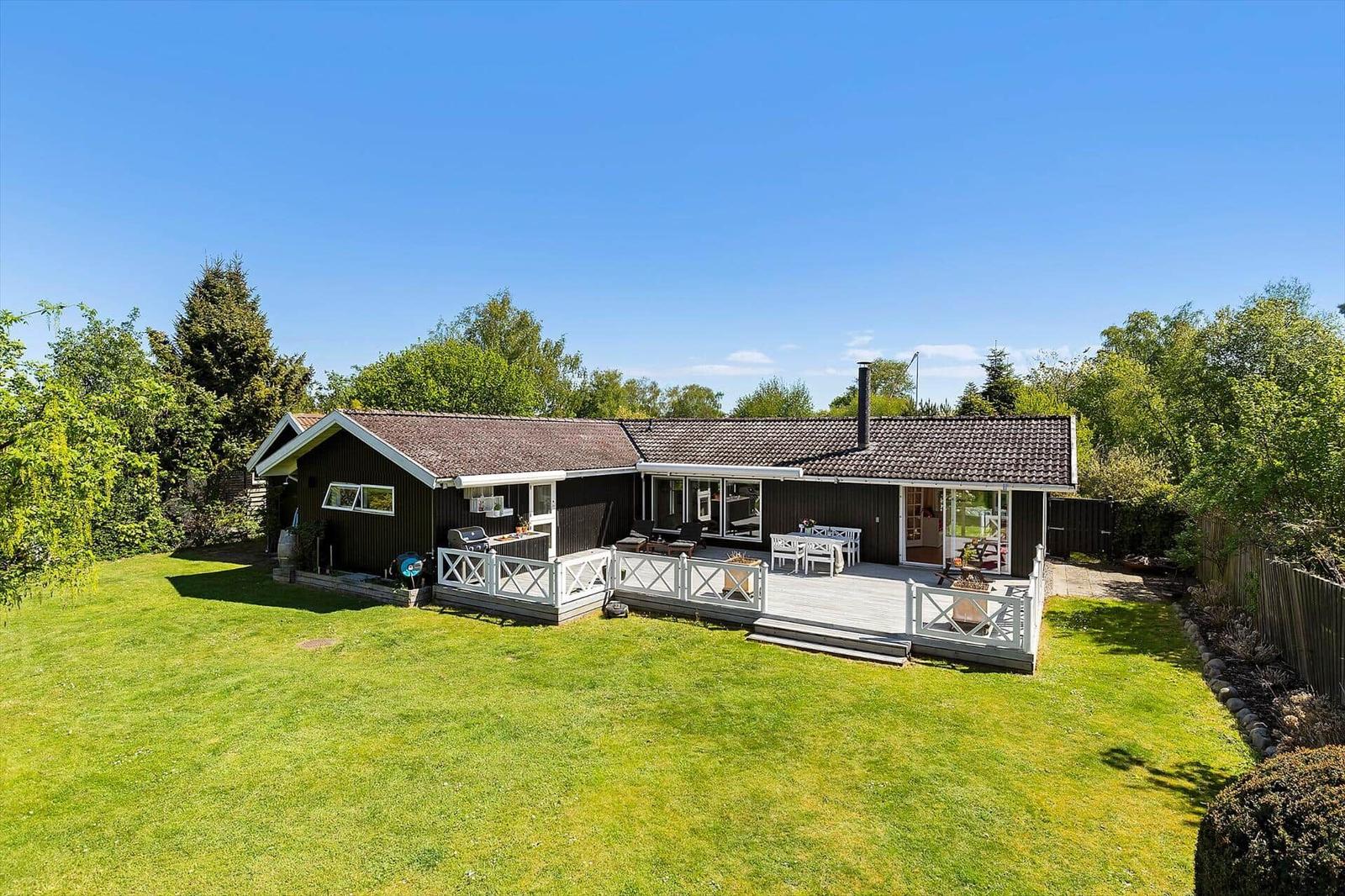 Ein Haus mit Terrasse, Grill und Garten unter blauem Himmel.