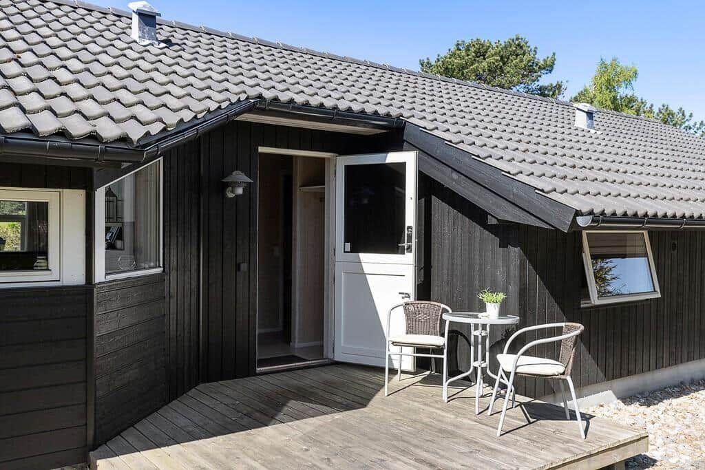 Haus mit Holzveranda, weiße Tür und Tisch mit zwei Stühlen.
