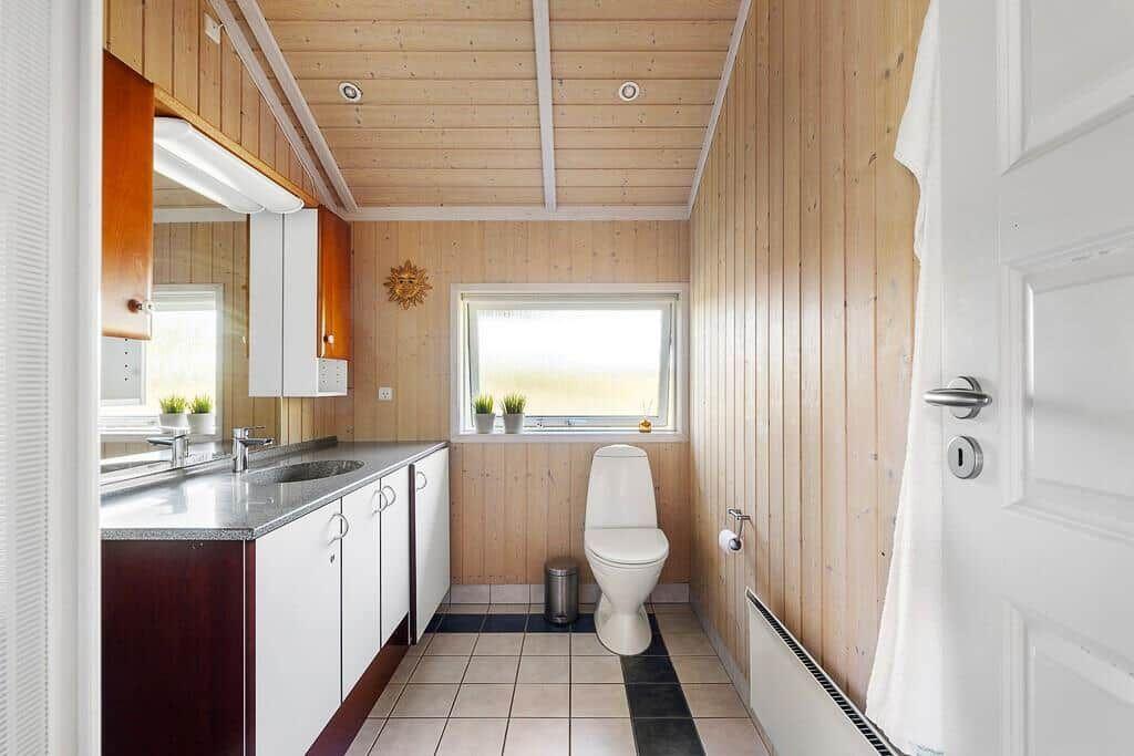 Badezimmer mit Holzwand, Waschbecken, Toilette und Fenster.