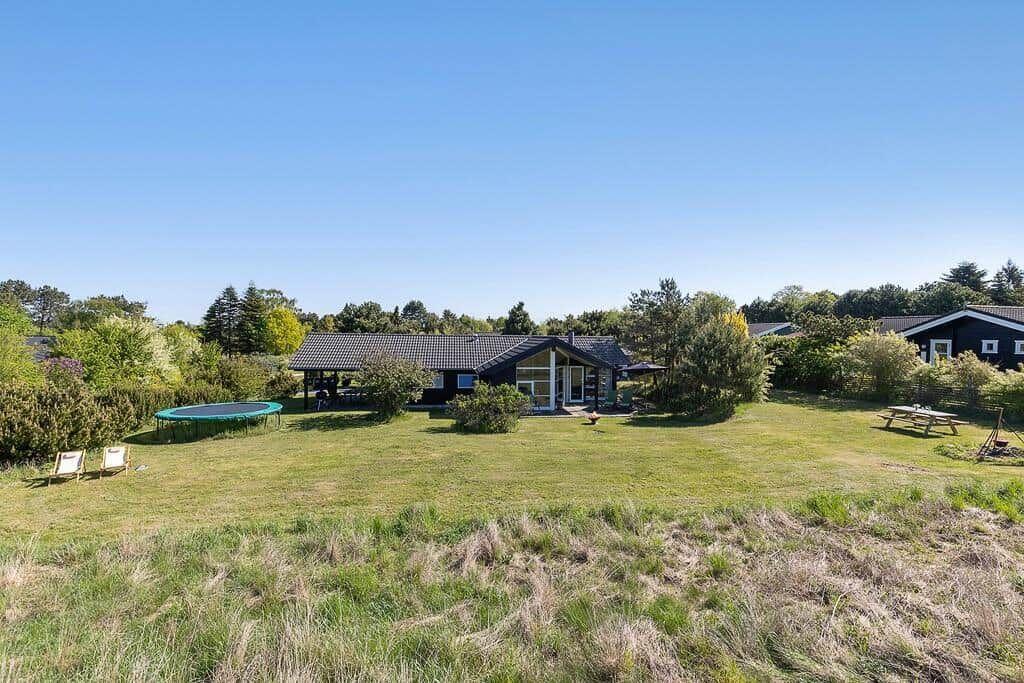Ein Haus mit großem Garten, Trampolin und Picknicktisch unter blauem Himmel.