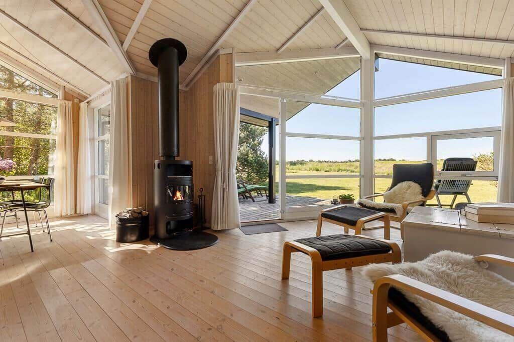 Wohnraum mit Holzfußboden, Kamin und großem Fensterblick auf die Landschaft.