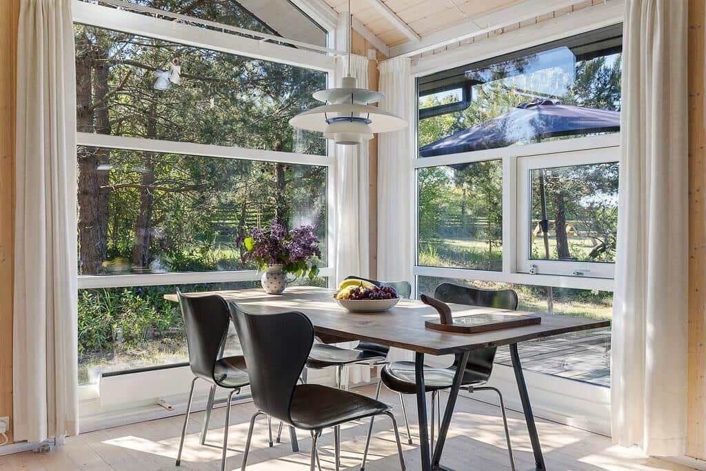 Essbereich mit Tisch und Stühlen. Große Fenster bieten Blick auf Wald und Terrasse.