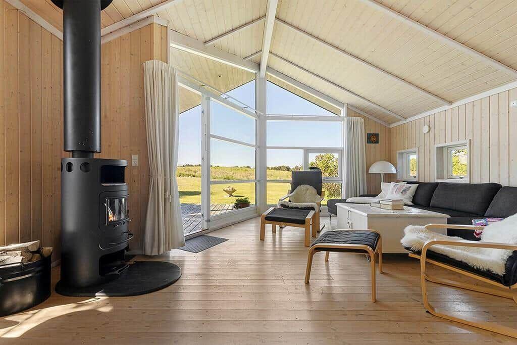 Wohnraum mit Holzwand, Kaminofen und großem Fensterblick auf Grasland.