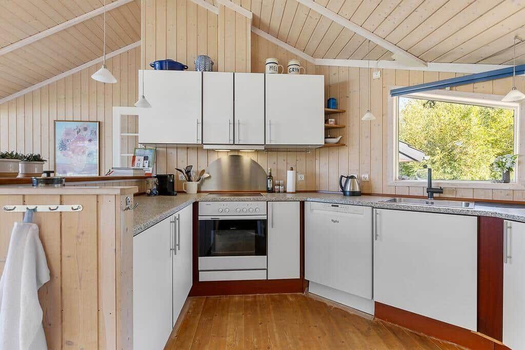 Küche mit weißen Schränken, Holzdecke und Fenster zum Garten
