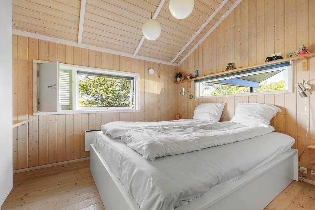 Schlafzimmer mit Holzwand, Bett und Fenstern.