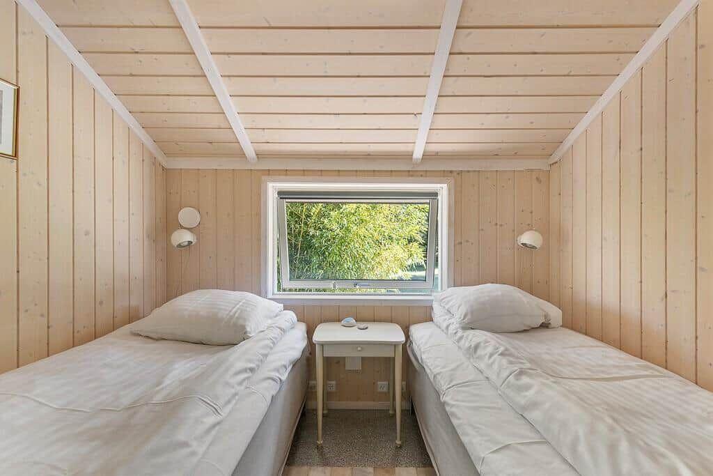 Zwei Einzelbetten mit weißer Bettwäsche stehen unter einem Holzdach.