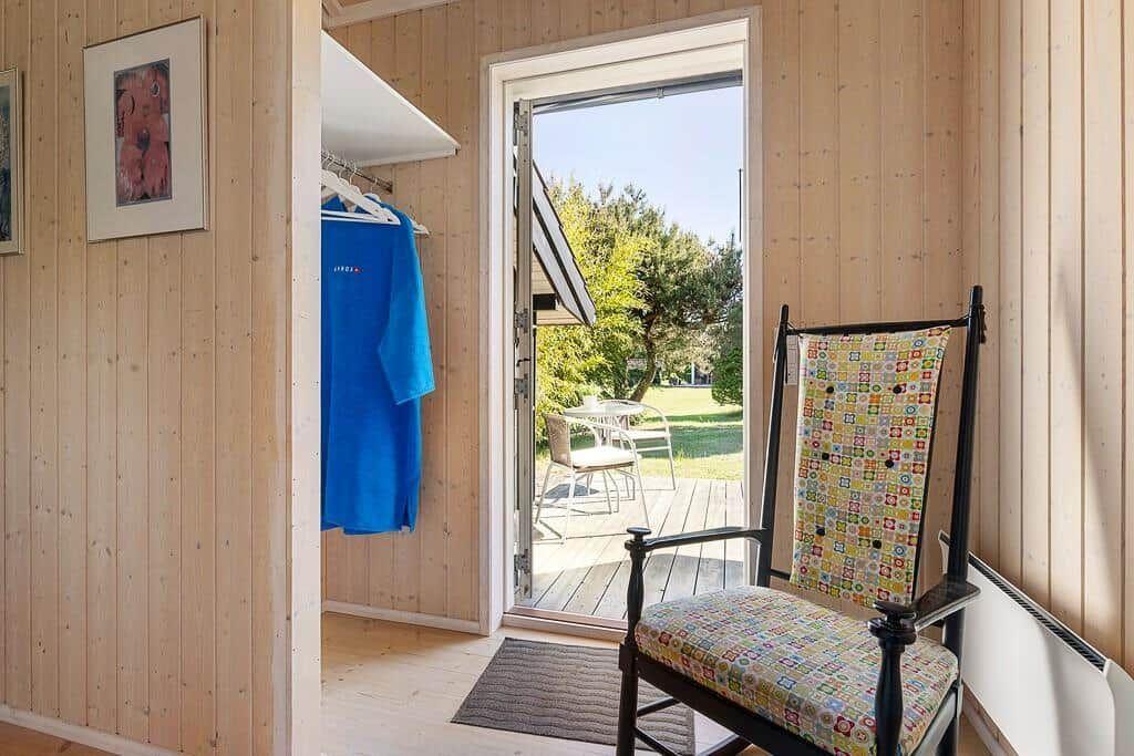 Raum mit Holzwand, Stuhl mit buntem Stoff, Kleiderständer und Tür zum Balkon.