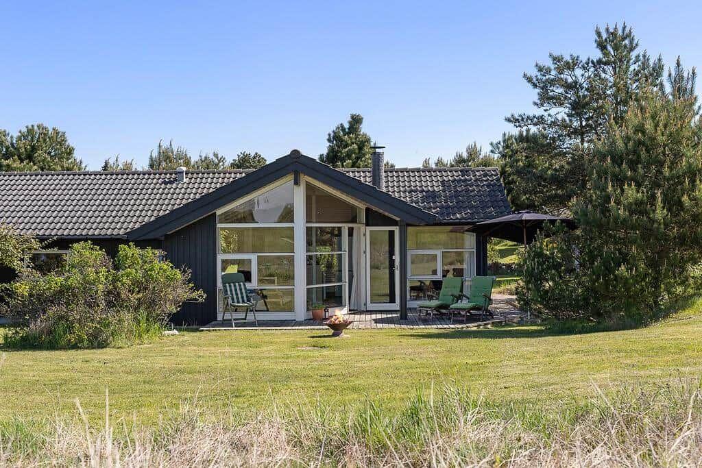 Moderne Villa mit großem Garten und Terrasse. Grüne Sitzgelegenheiten und Bäume umgeben das Haus.