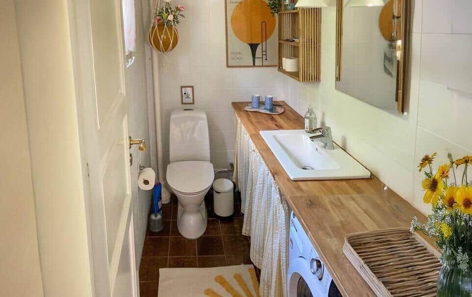Badezimmer mit Waschmaschine, Waschtisch und Toilette. Holzoberfläche und Spiegel sichtbar.