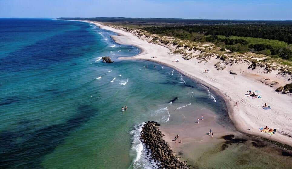 Strand mit klarem Wasser und Sand, Menschen baden und entspannen.