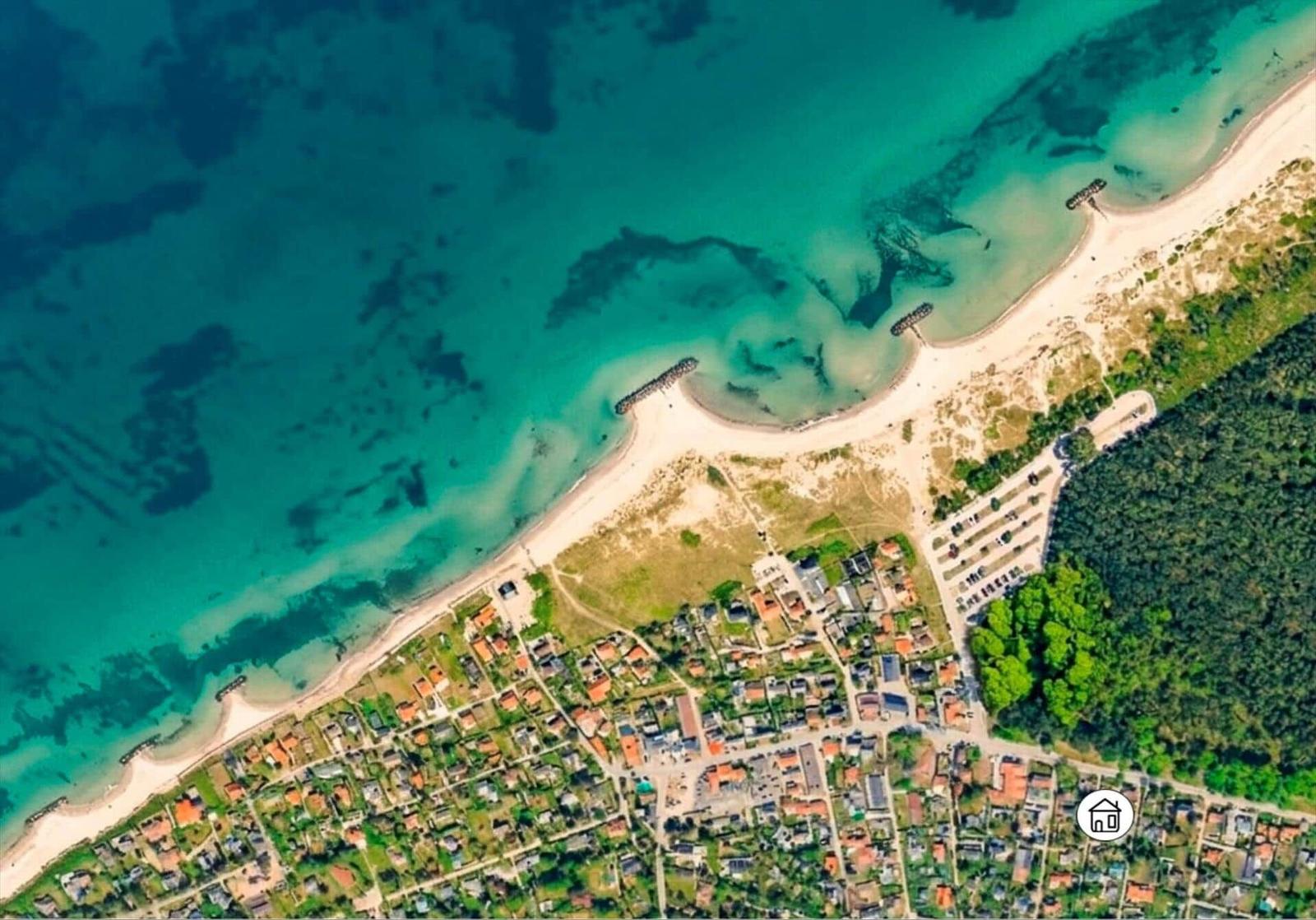 Aerial view of a coastal village with sandy beach, turquoise water, and surrounding greenery.