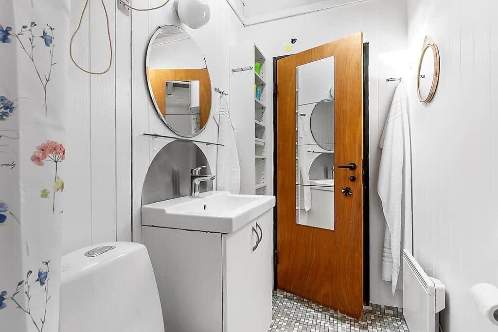 Badezimmer mit Waschbecken, Spiegel und Dusche. Holztür und Mosaikboden.