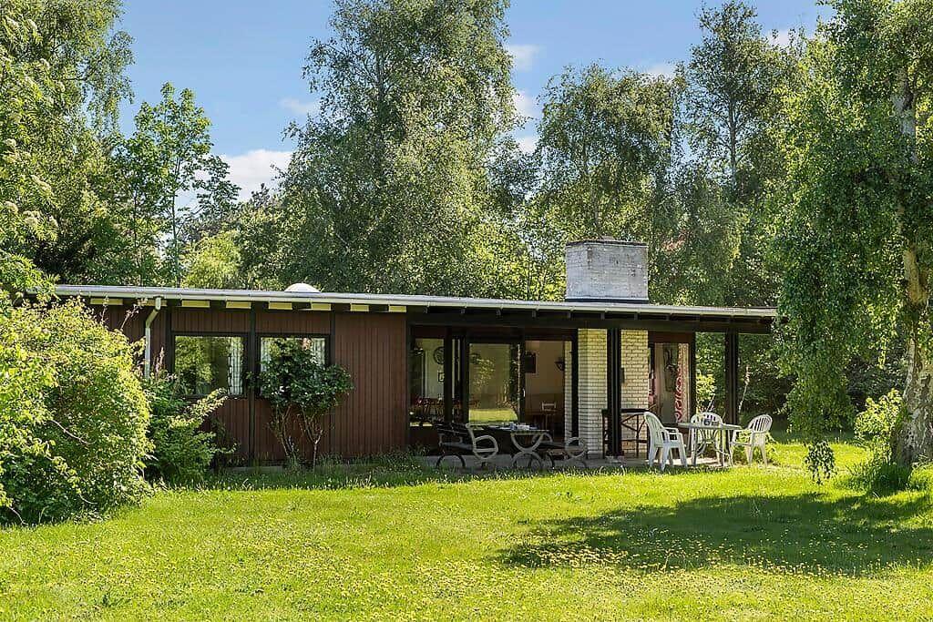 Moderne Hütte mit Terrasse, Garten und Bäumen. Tisch und Stühle draußen.