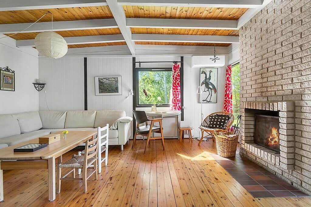 Wohnzimmer mit Kamin, Holzboden und großem Fenster mit Blick auf Grün.