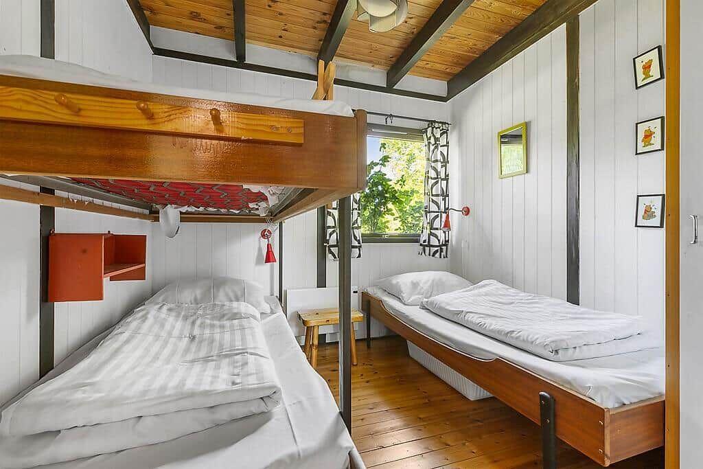 Zimmer mit Doppelstockbett, Einzelbett und Fenster mit Blick auf Grün.