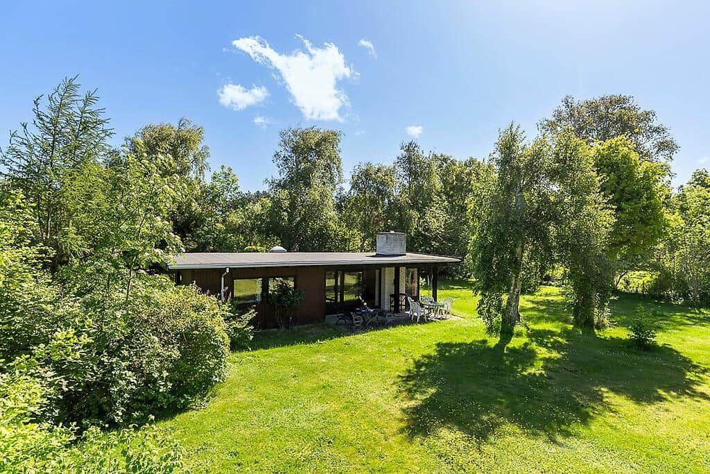 Ein Haus mit Terrasse und Garten umgeben von Bäumen unter blauem Himmel.