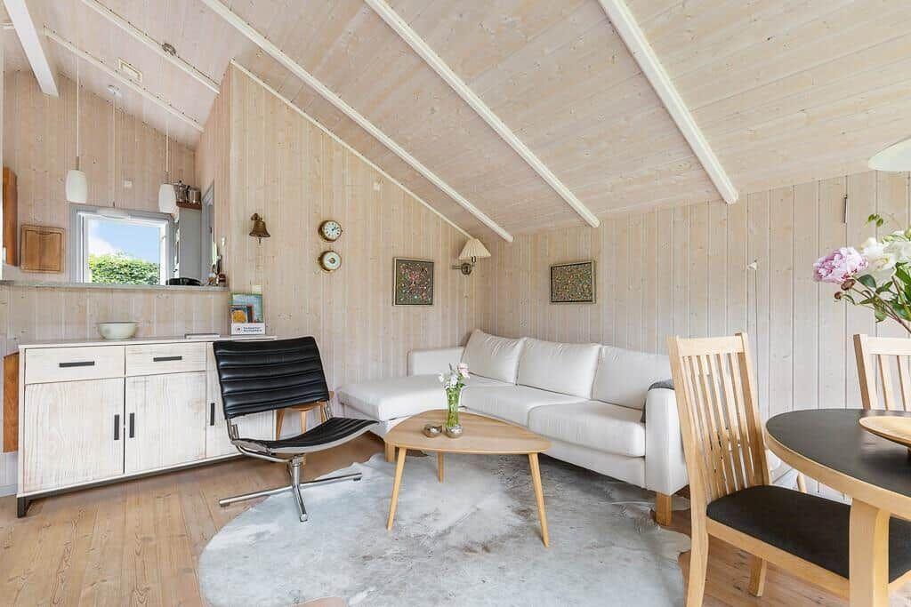 Wohnbereich mit Sofa, Tisch und Stühlen. Holzwände und -decke. Fenster mit Blick draußen.