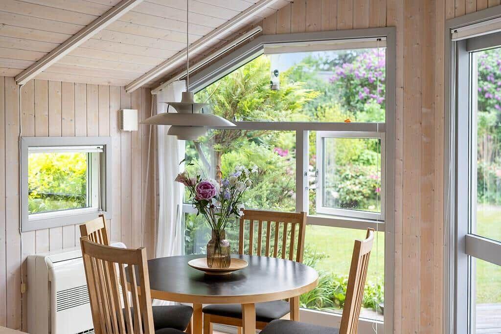 Rundtisch mit vier Stühlen vor großem Fenster mit Gartenblick.