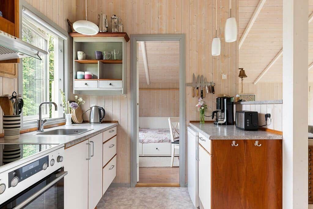 Küche mit Arbeitsplatte, Spüle und Fenster. Durchgang zu Schlafzimmer mit Bett.