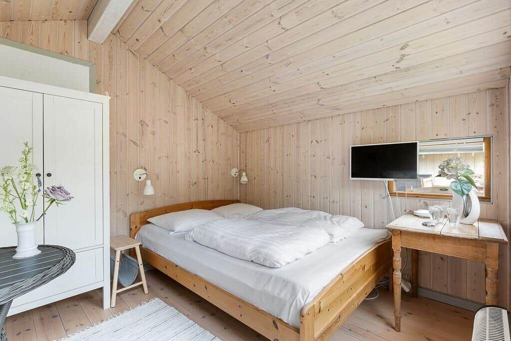 Schlafzimmer mit Holzwand, Bett, Schreibtisch und Fernseher
