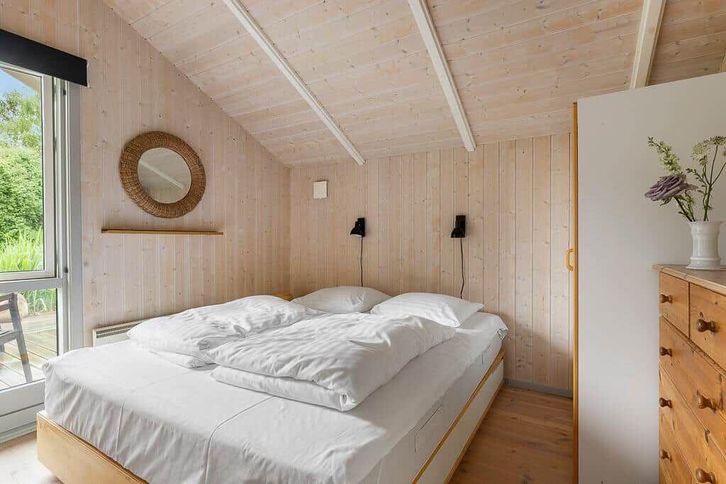 Schlafzimmer mit Holzwand, Bett und Fenster zur Außenterrasse.