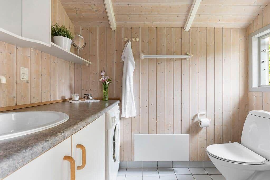 Badezimmer mit Holzwand, Waschbecken, Toilette und Badewanne.