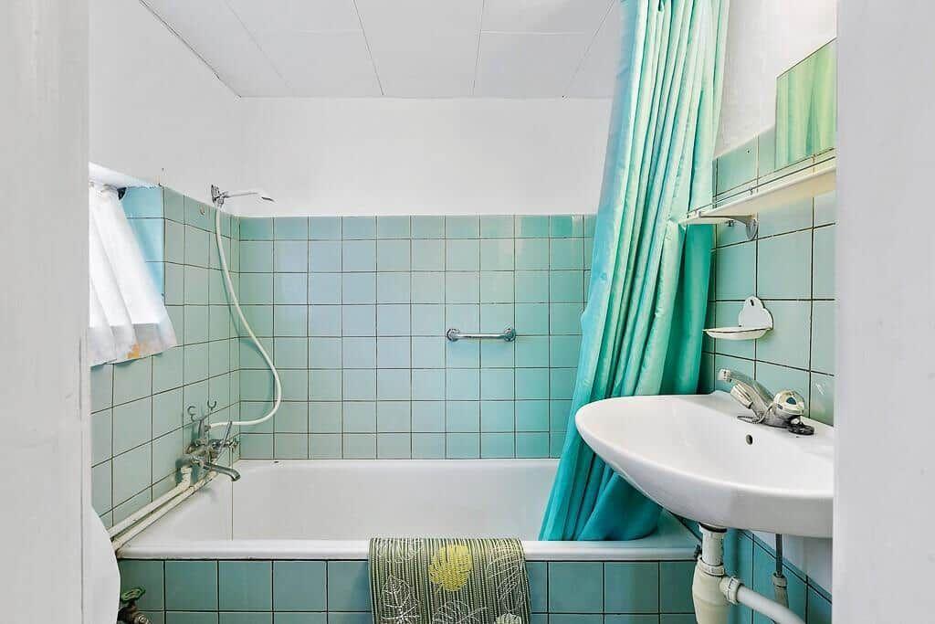 Badezimmer mit Badewanne, Duschbrause und Waschbecken mit grüner Fliesenwand.