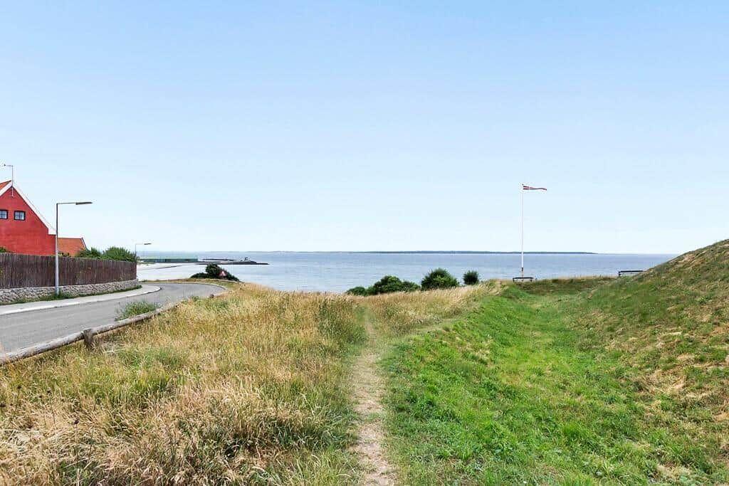 Weg führt entlang Grasfläche zum Wasser. Rote Gebäude und Flagge sind sichtbar.