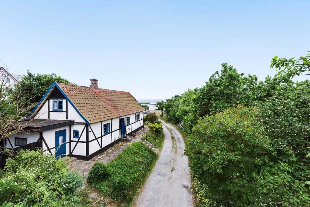 Ein weißes Fachwerkhaus mit blauen Fenstern und Tür, umgeben von Bäumen und einem Weg.